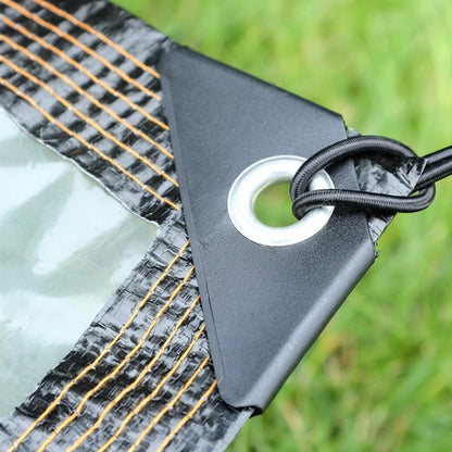 Close-up of a clear tarp with a reinforced black corner, metal grommet, and black elastic attachment cord.